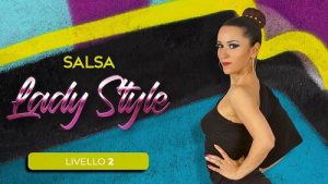 Una donna in abito nero posa con sicurezza su uno sfondo colorato di graffiti. Il testo recita Salsa Lady Style e Livello 2, con corsi di danza online della Freedance Academy.
